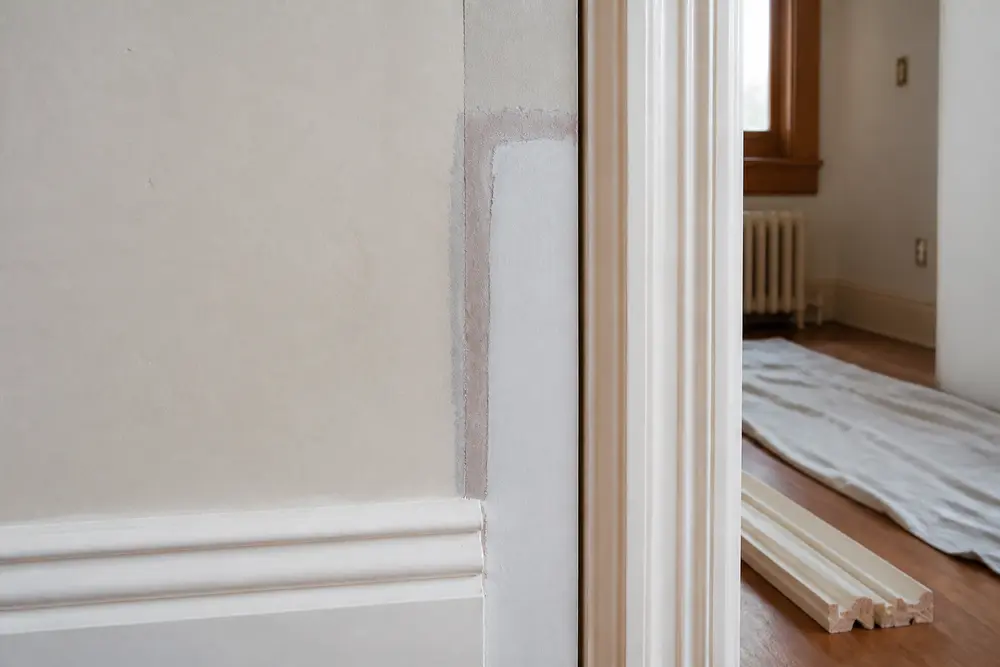 A bounded wall and trim repair nears completion while the surrounding floor and doorway remain protected.