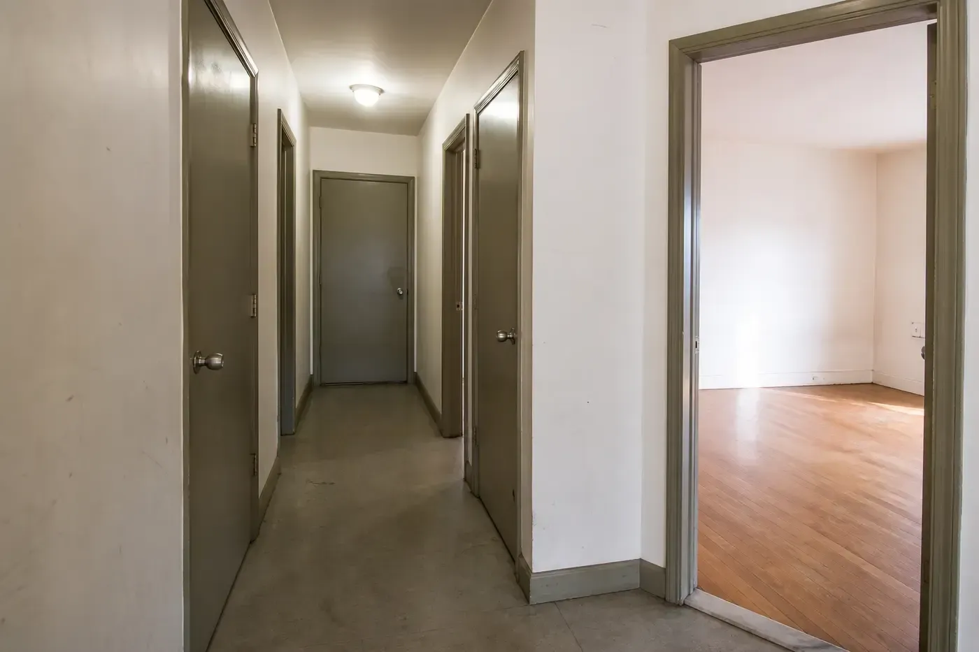 A multi-room rental unit hallway with several doors and an open room ready for a coordinated repair walkthrough.