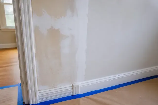 A wall shows feathered surface preparation, primer and protected trim before the finish coat.